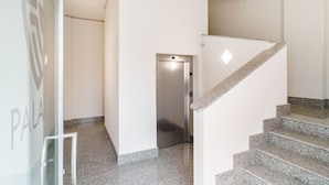 A modern interior with a staircase, a glass door with a logo, and a metallic elevator. - GuestHost - Scaringi Palace Trani - Room 10A (Trani)