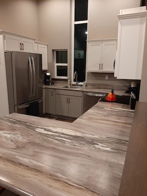 A modern kitchen with white cabinets, a stainless steel refrigerator, a sink, and a countertop with a marble-like backsplash.