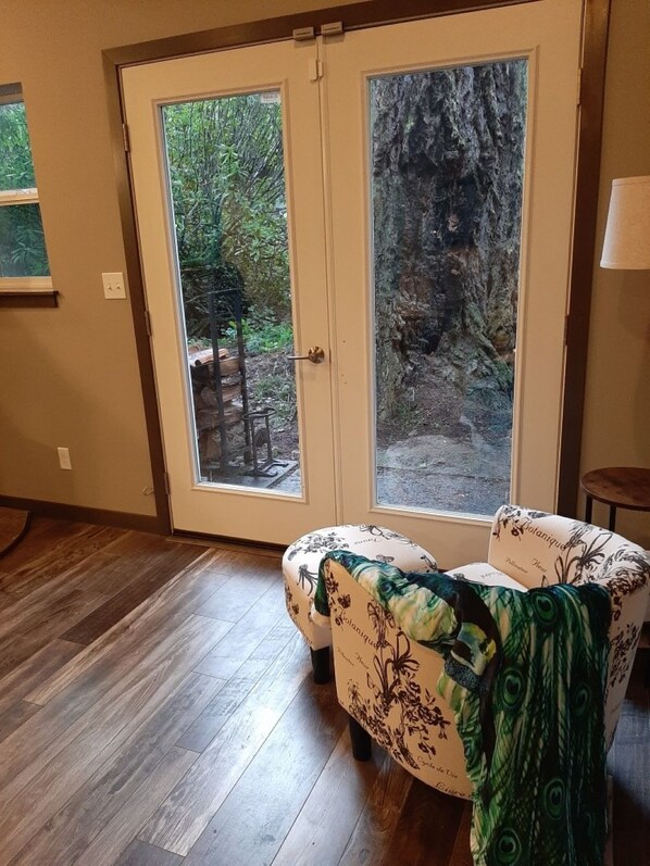 A room with a wooden floor, a door with a glass panel, and a chair with a peacock pattern.