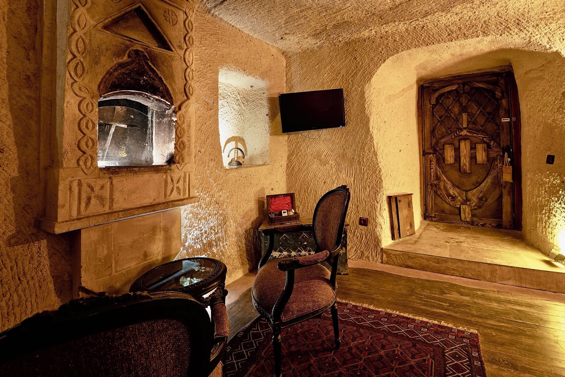 A cozy room with a fireplace, a television mounted on the wall, a wooden door, and a patterned rug.