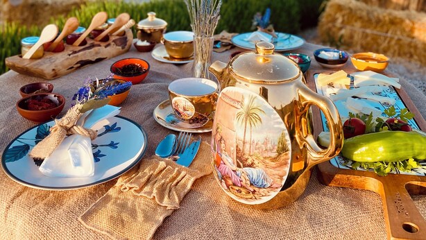 Ein Picknick mit verschiedenen Speisen, einem Teekessel und einer rustikalen Tischdecke in einer malerischen Naturkulisse mit Felsformationen und Heißluftballons im Hintergrund.