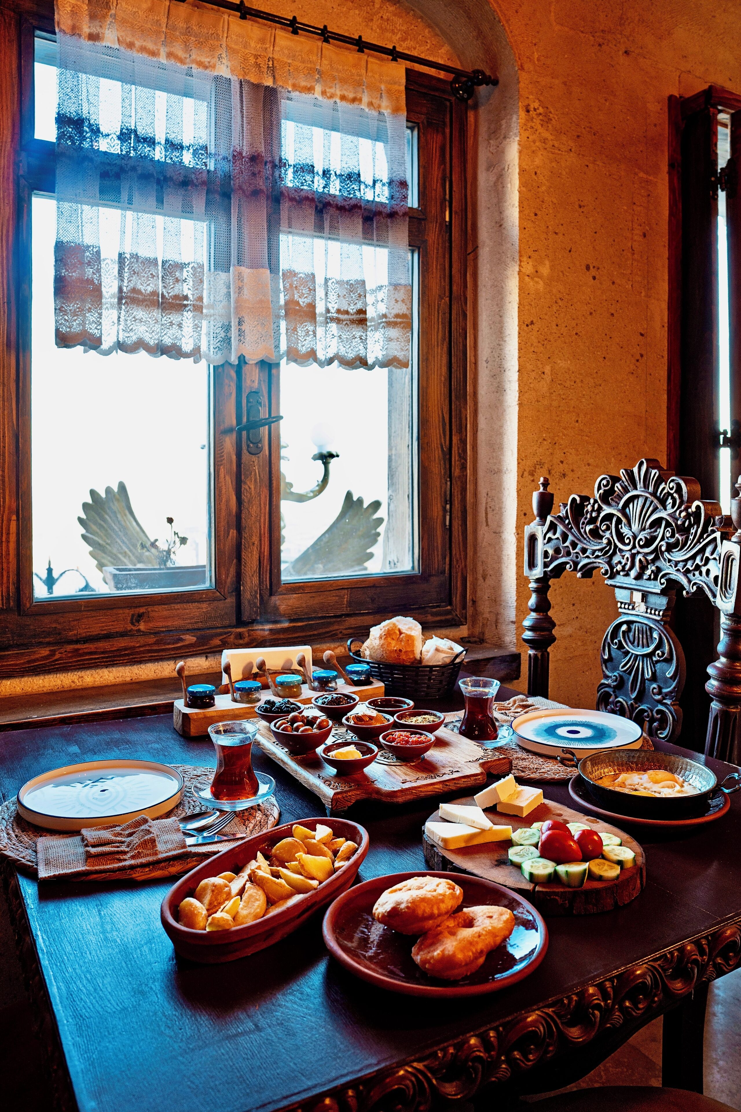 Une table à manger, ornée de différents plats, et une chaise décorative, le tout placé devant une fenêtre agrémentée de rideaux en dentelle.