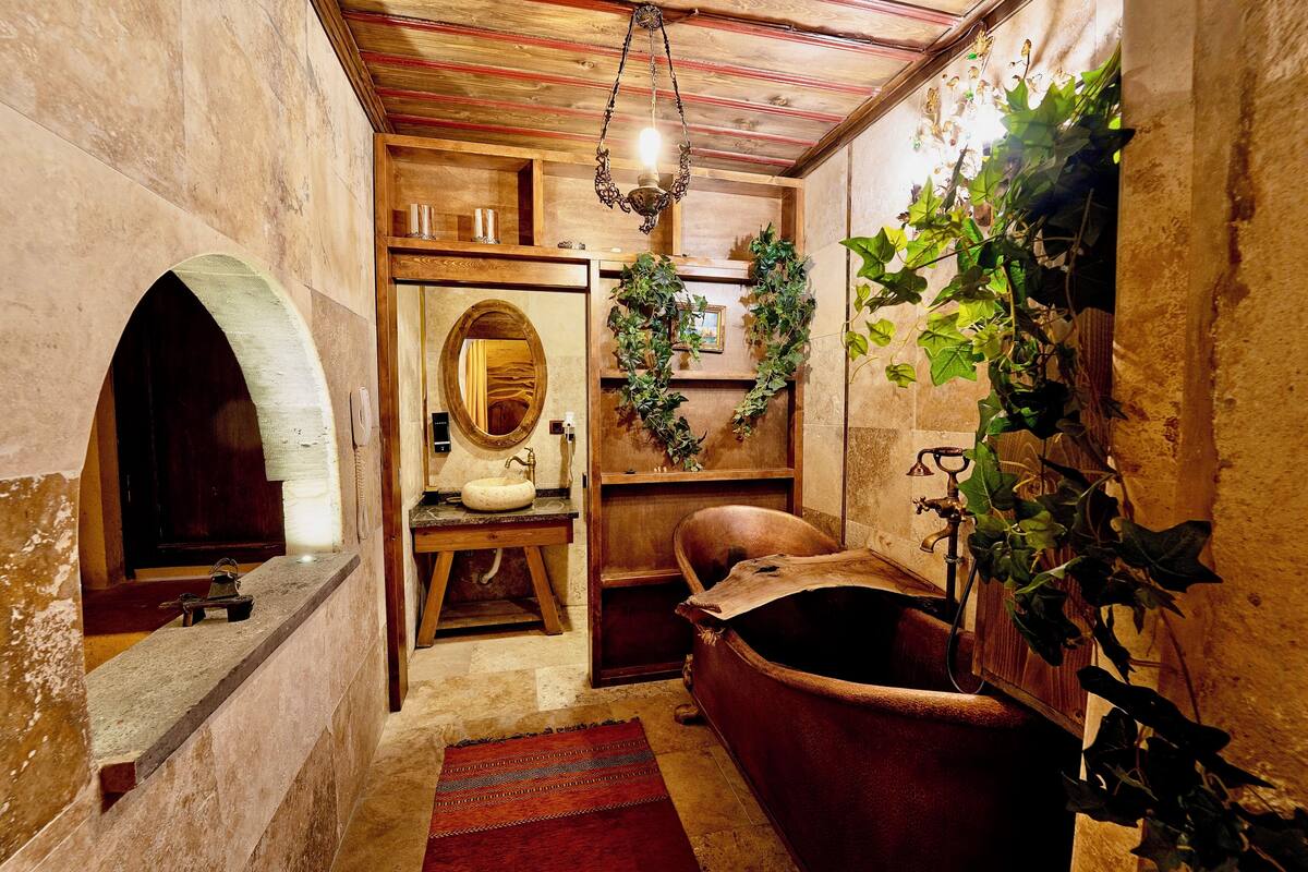 A rustic bathroom with a wooden bathtub, a stone sink, and a mirror.