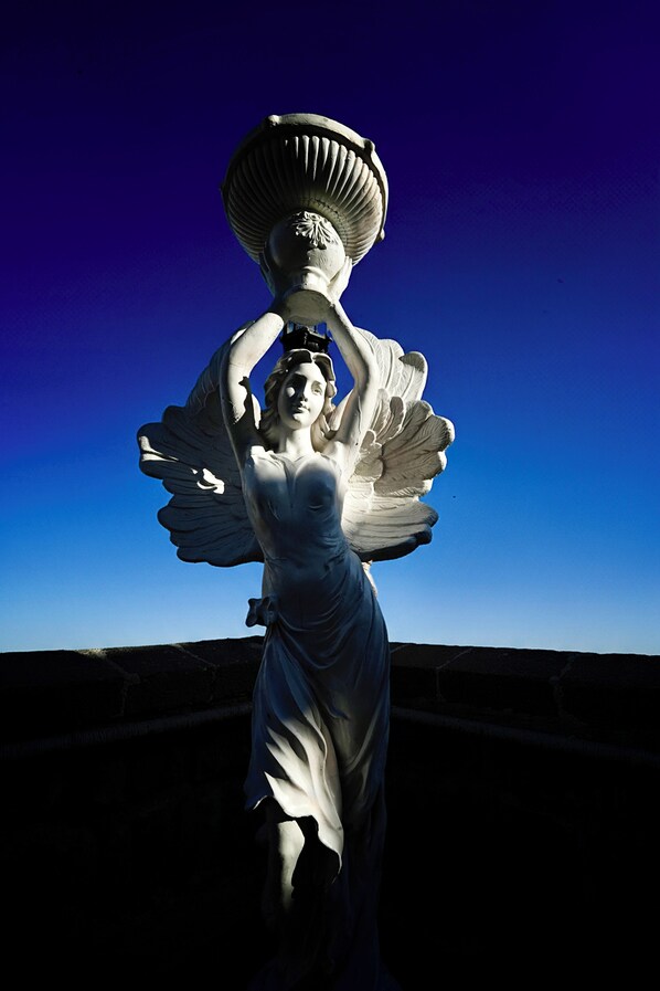 Una estatua de una mujer sosteniendo un gran jarro, con un cielo azul despejado de fondo.