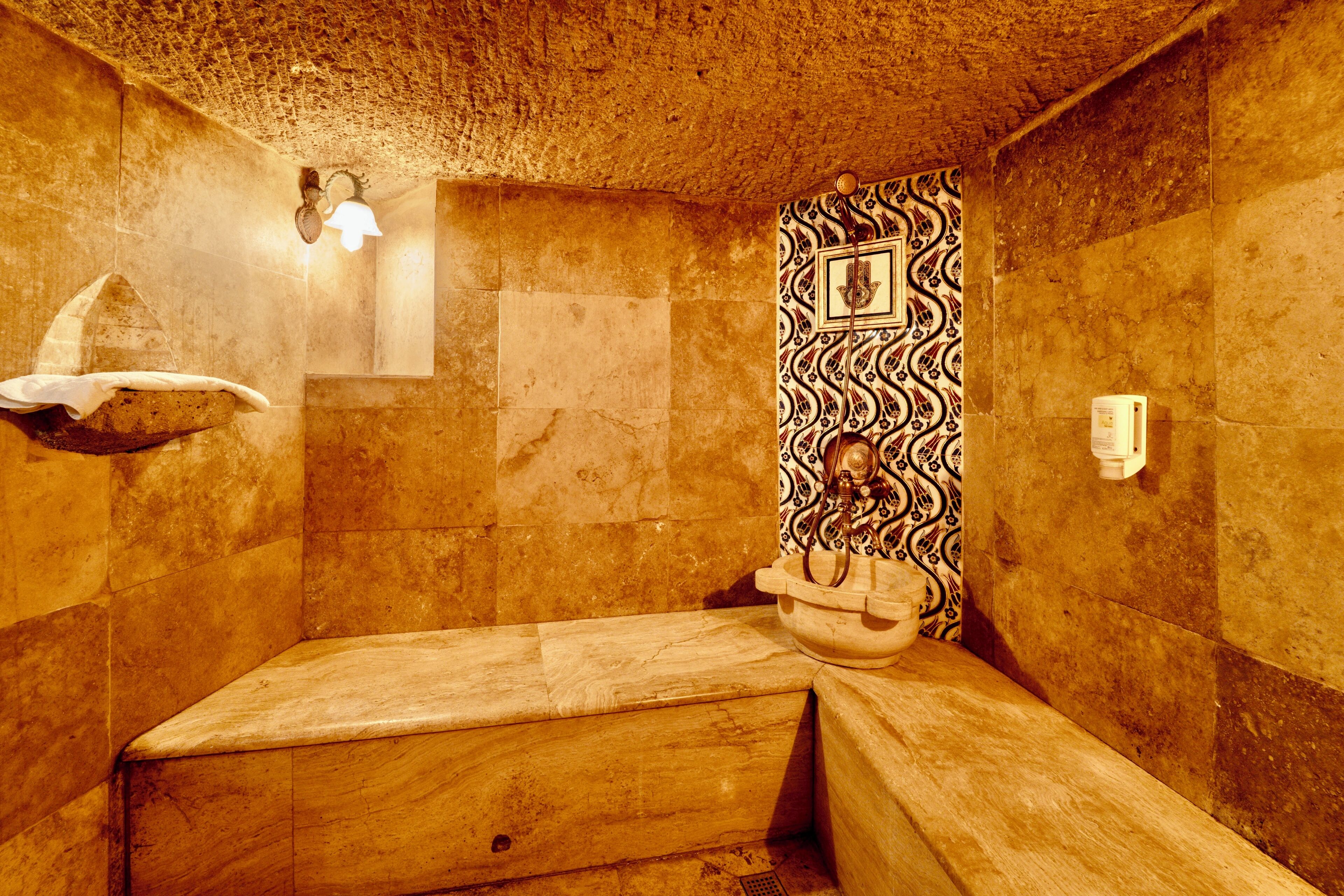 Ein Badezimmer mit Steinwänden, einer Badewanne, einem wandmontierten Waschbecken und einem dekorativen Fliesenspiegel.