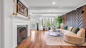 A spacious living room with hardwood flooring, a fireplace, a large sectional sofa, and a modern wall design. - Mid-Century Bungalow in the Heart of Buckhead! (Atlanta)