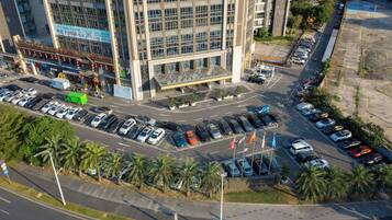 A multi-story hotel with a modern glass facade, a parking lot with various vehicles, and a street with palm trees.