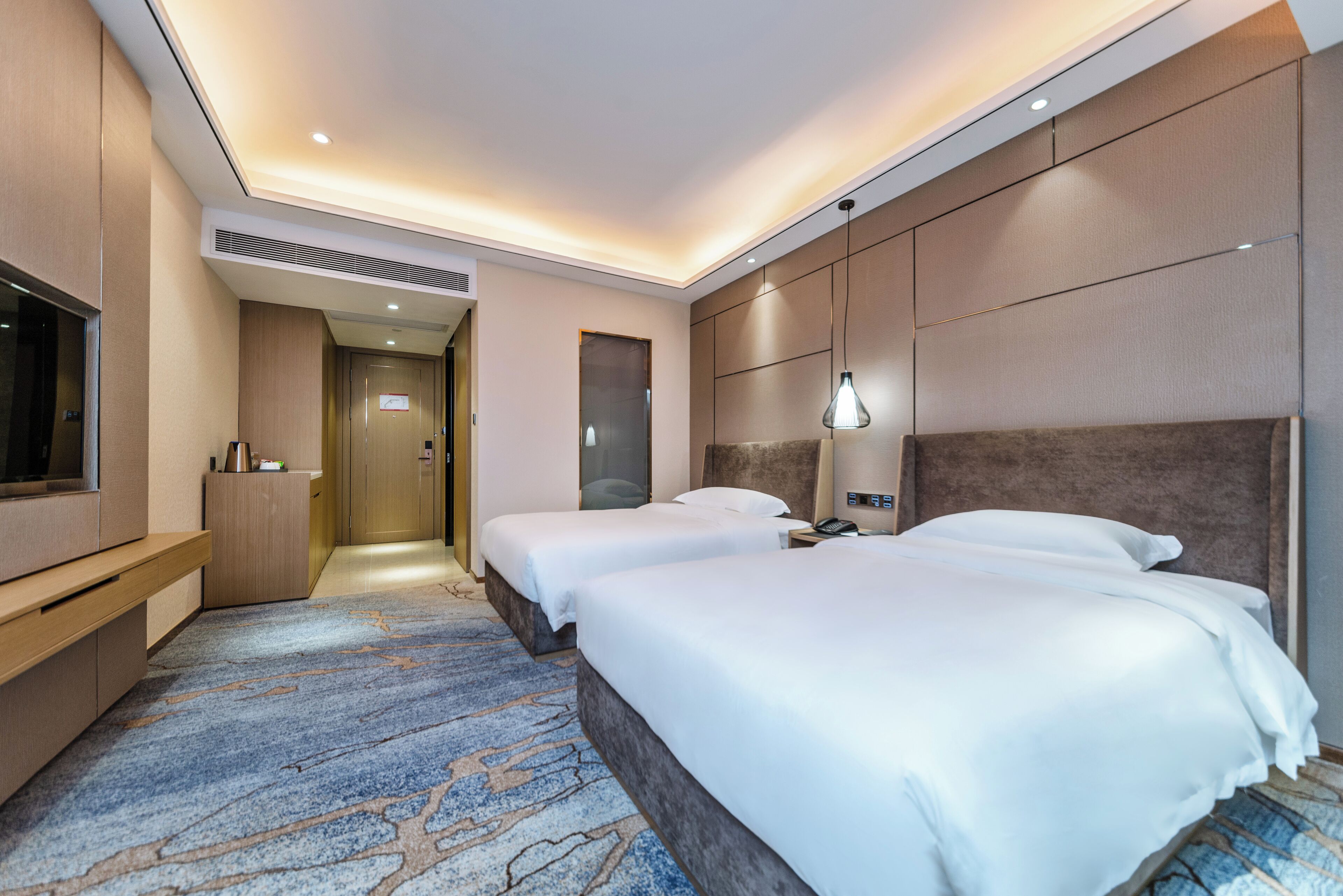 A hotel room with two beds, a TV, a desk, and a carpeted floor.