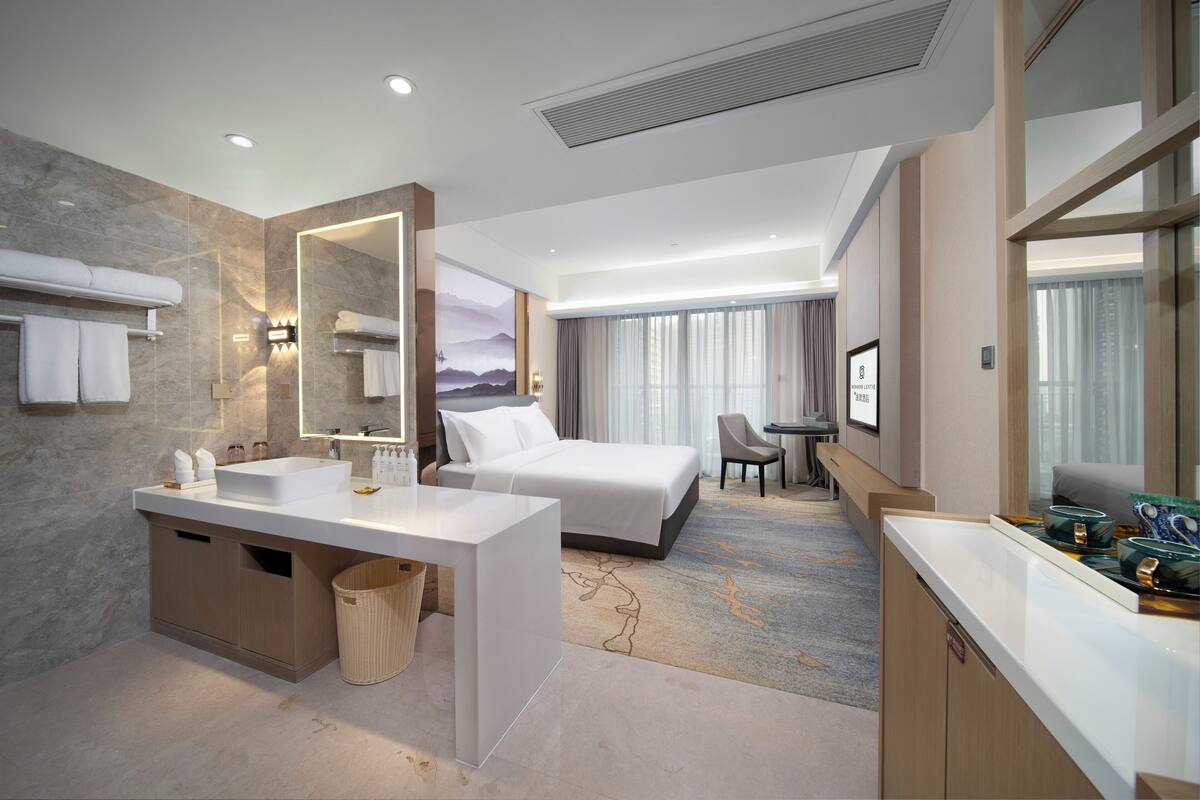A modern hotel room with a large bed, a desk, a chair, and a small table.