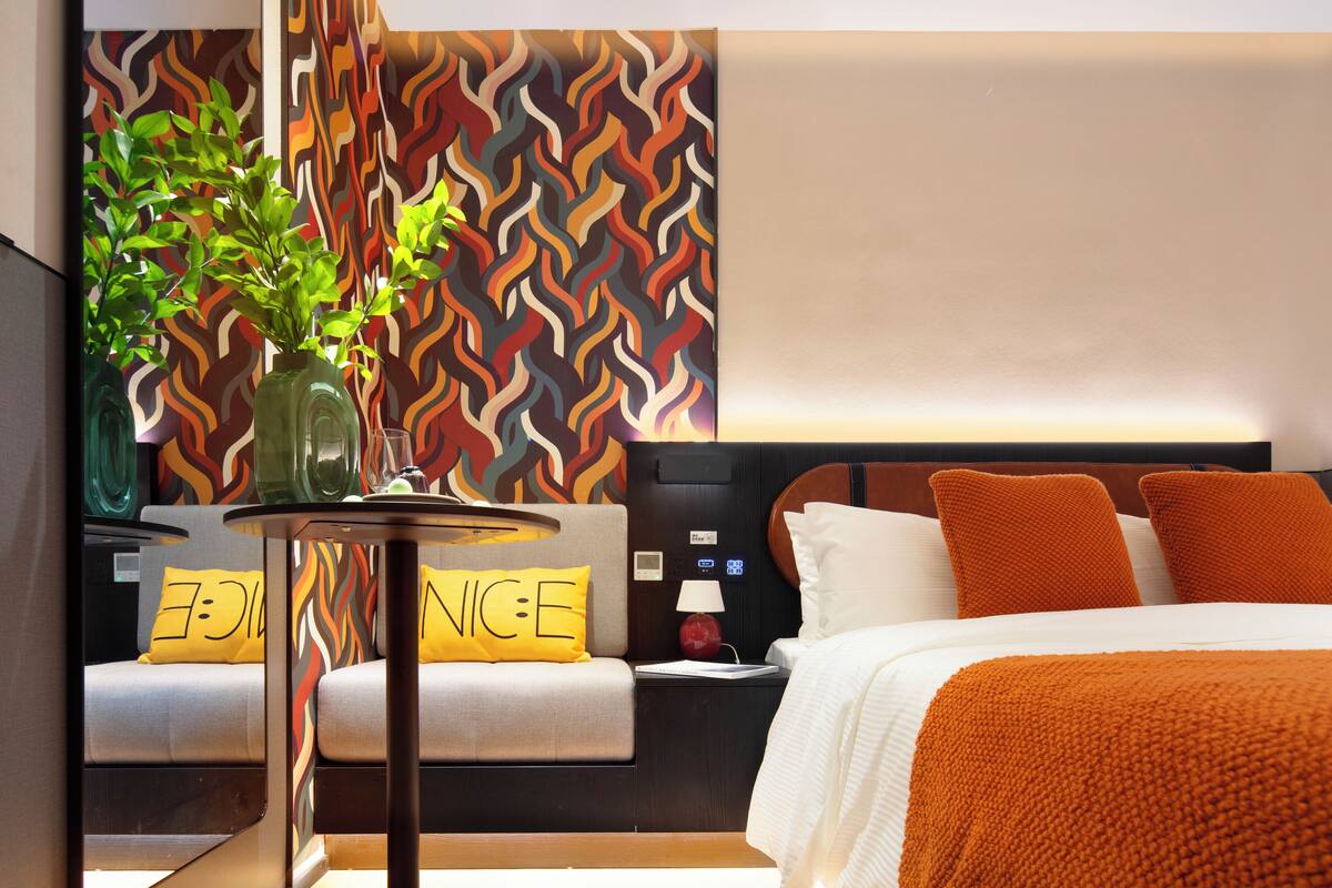 A modern hotel room with a bed, a bedside table with a lamp, and a wall with a wavy pattern.