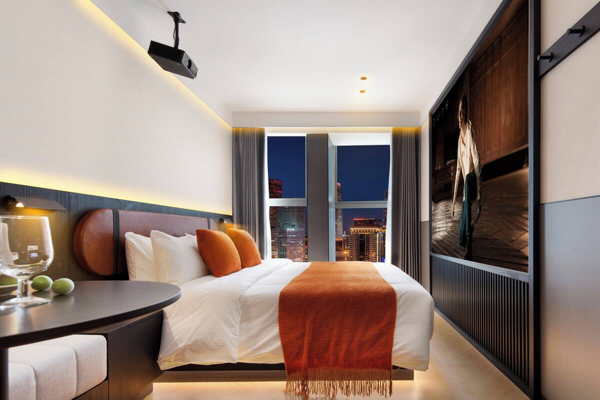 A modern hotel room with a large bed, a desk, and a city view.