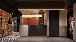 Un espace d’accueil d’hôtel au design moderne, comprenant un comptoir d’accueil, un mur orné d’une fresque colorée et un sol carrelé.