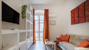 A modern living room with a sofa, a coffee table, a TV mounted on the wall, and a balcony door. - GuestHost - Lovely apartment for 4 people, located just 200 meters from the sea. The accommodation boasts every comfort e a palette of warm colors that create a welcoming and cheerful environment. Ideal location: just 5 minutes walk from Corso Vittorio E (Bari)