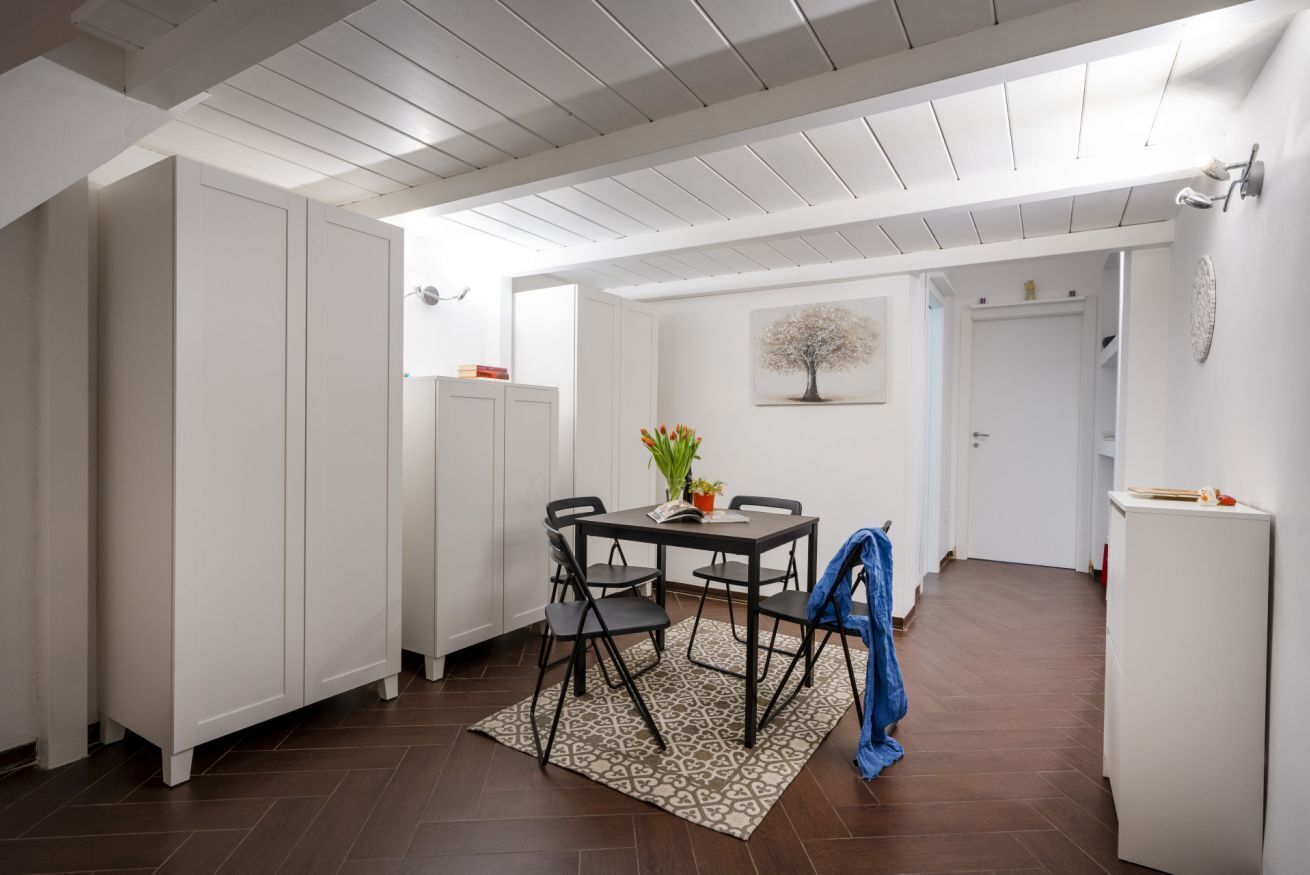 A compact kitchen with white cabinetry, a dining table with chairs, a patterned rug, and a painting on the wall.