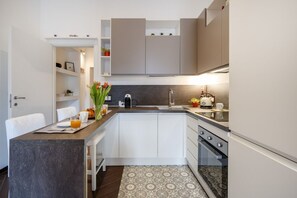 Une cuisine moderne avec des meubles blancs, un four encastré et un coin repas comprenant une table et des chaises.