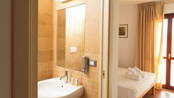 Un baño de hotel con lavamanos, espejo y panel de control de la ducha.