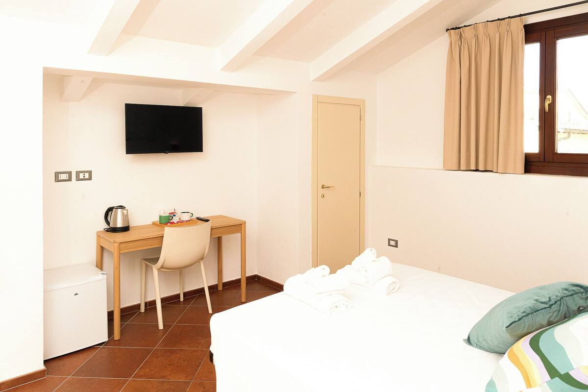 A bedroom with a bed, a desk with a chair, a television, and a door.