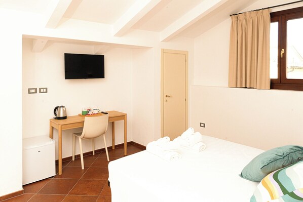 A bedroom with a bed, a desk with a chair, a television, and a door. - LA ROCCA RELAIS (Serravalle Pistoiese)