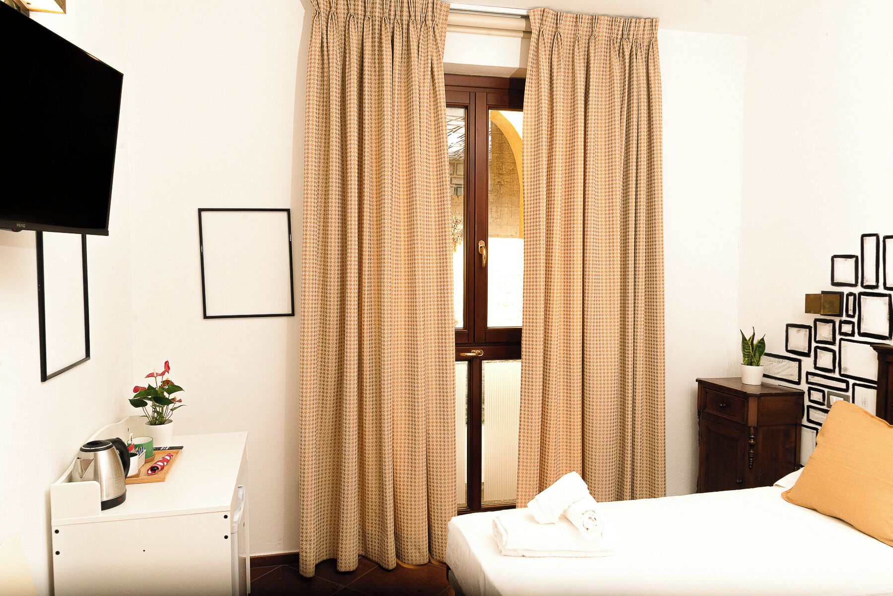 Une chambre d’hôtel avec un lit, une table de chevet, une télévision et une fenêtre avec des rideaux.