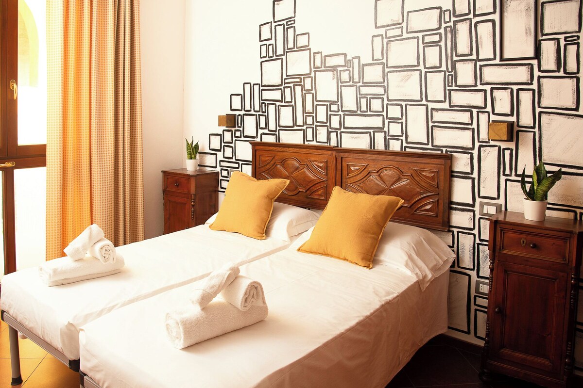 A double bed with two pillows, a wooden headboard, and a patterned wall.