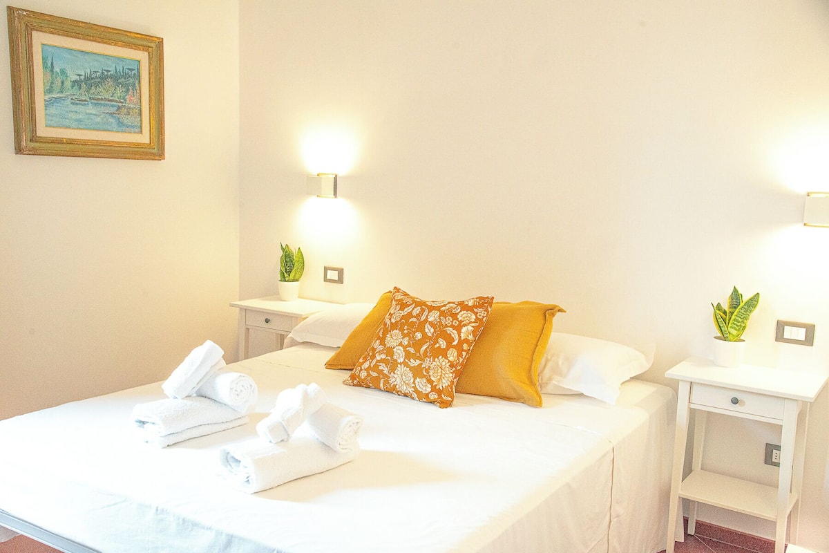 A hotel room with a bed, white towels, a painting on the wall, and two bedside tables with lamps.