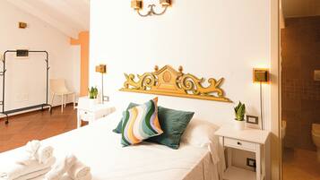 A hotel room with a bed, a bedside table, a nightstand, a wall-mounted light fixture, and a towel rack.
