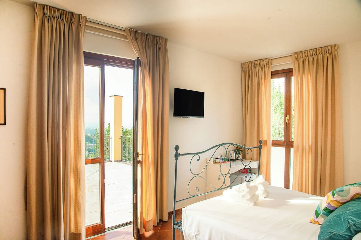 A bedroom with a bed, a television on the wall, and curtains on the windows.