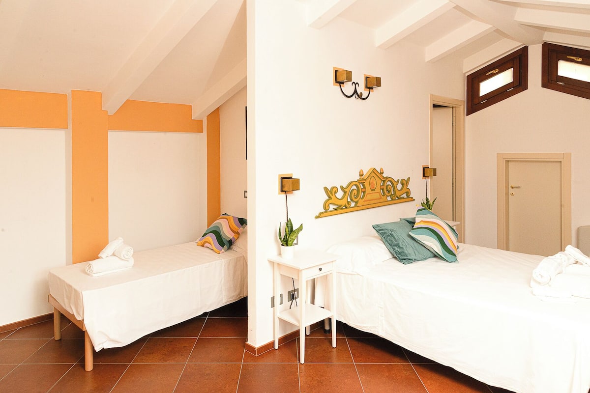 A hotel room with two single beds, a small table with a plant, and a decorative headboard.