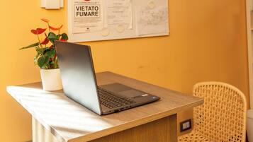 A laptop on a wooden table with a potted plant beside it.