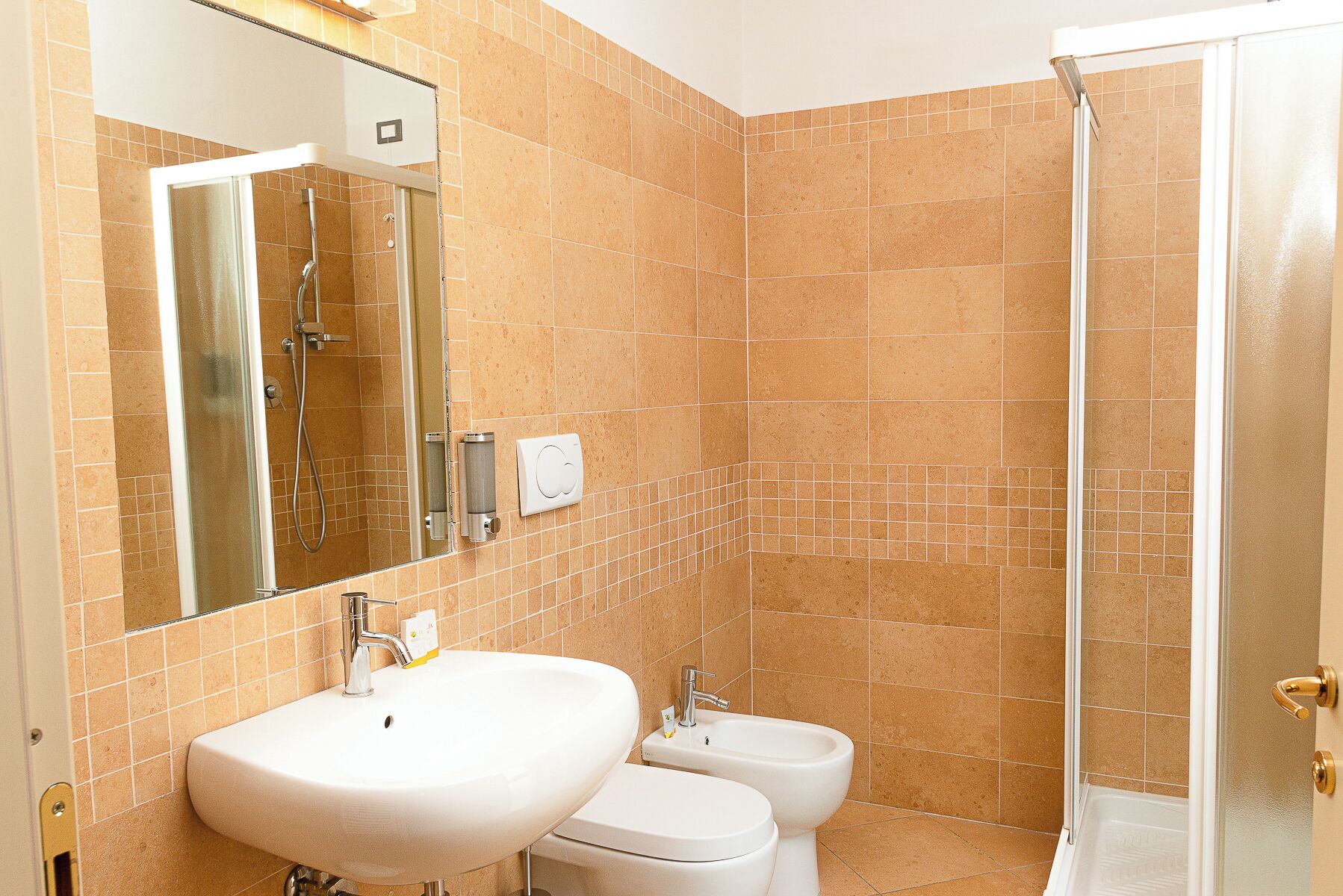 A bathroom with a large mirror, two sinks, a bidet, and a shower.