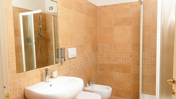 A bathroom with a large mirror, two sinks, a bidet, and a shower.