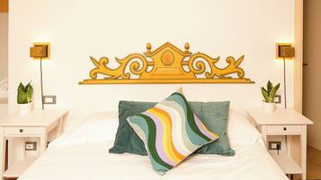 Una cama con un almohadón a rayas de colores, un cabecero decorativo, mesitas de noche con lámparas y plantas en macetas.