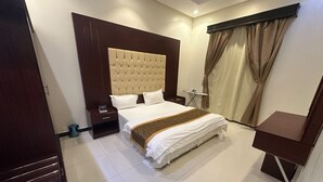 A hotel room with a large bed, a wooden headboard, a bedside table, a small table with a chair, and a window with curtains. - Luluat Althuraya Serviced Apartments (Riyadh)