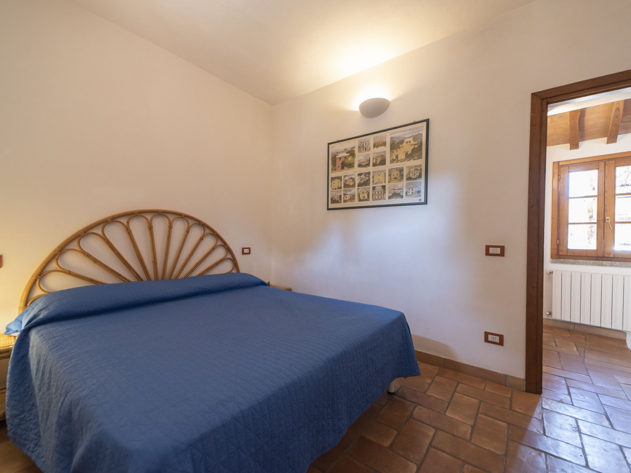 A bedroom with a bed, a wall-mounted picture, and a window with wooden shutters.