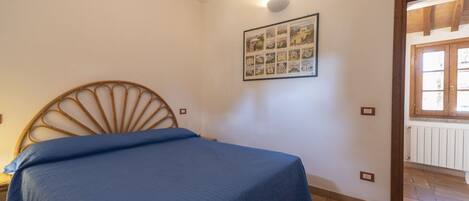 A bedroom with a bed, a wall-mounted picture, and a window with wooden shutters.