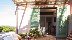 Eine Terrasse im Freien mit einem Holztisch, grünen Sitzgelegenheiten mit Polstern und Blick auf das Meer.
