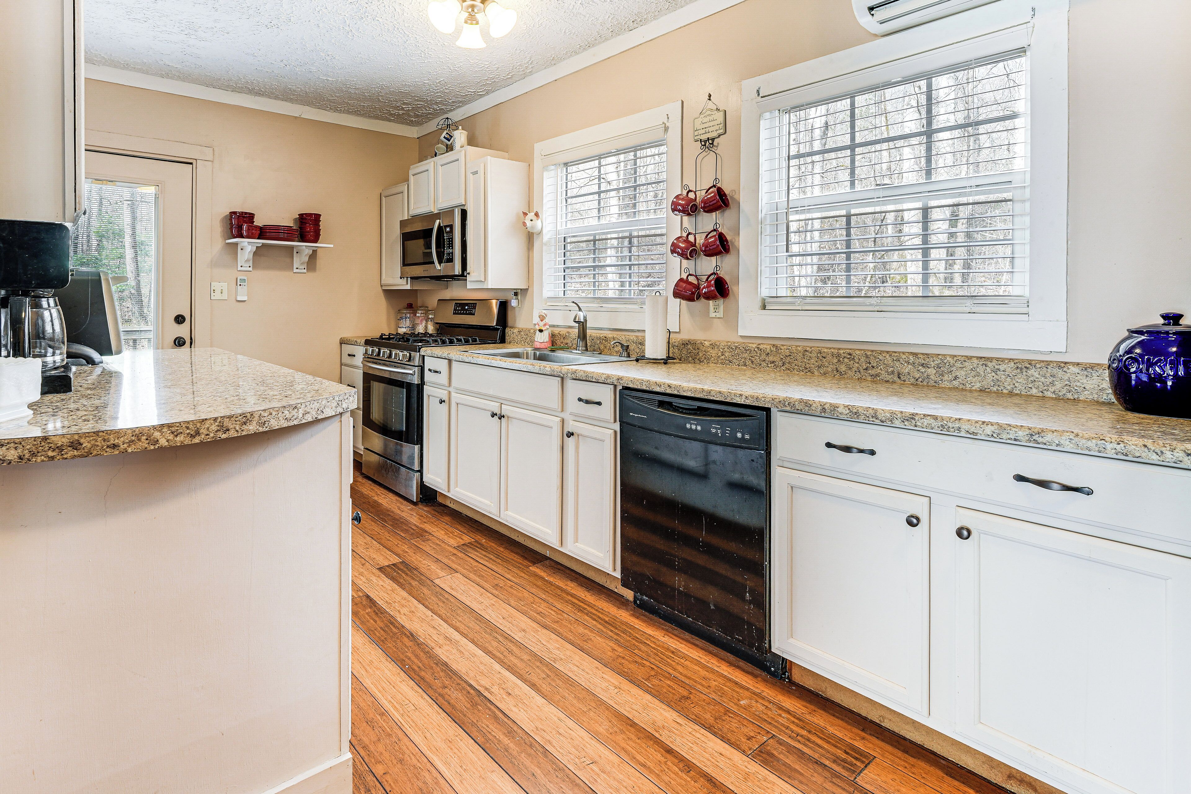 A kitchen with white cabinets, a granite countertop, a dishwasher, a microwave, and a stove.