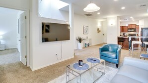 A modern living room with a flat-screen TV, a blue leather chair, and a glass coffee table.