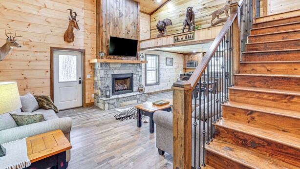 A log cabin interior with a stone fireplace, wooden staircase, and mounted animal heads. - Pet-Friendly Yard! Nature Escape in Forest City (Forest City)