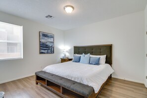 Een slaapkamer met een bed, een bankje, een nachtkastje, een lamp en kunstwerken.