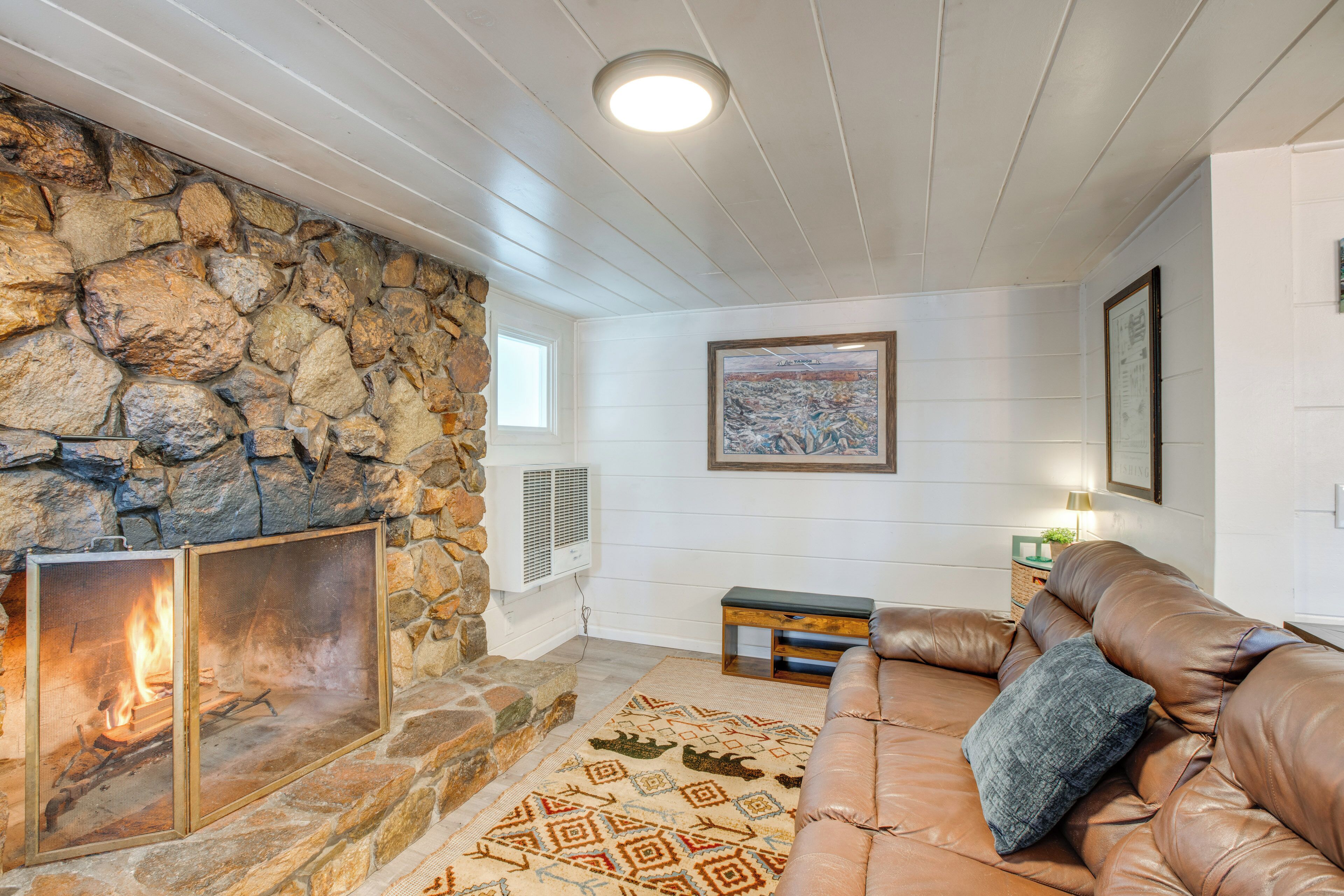 A cozy living room with a stone fireplace, a leather sofa, and a patterned rug.