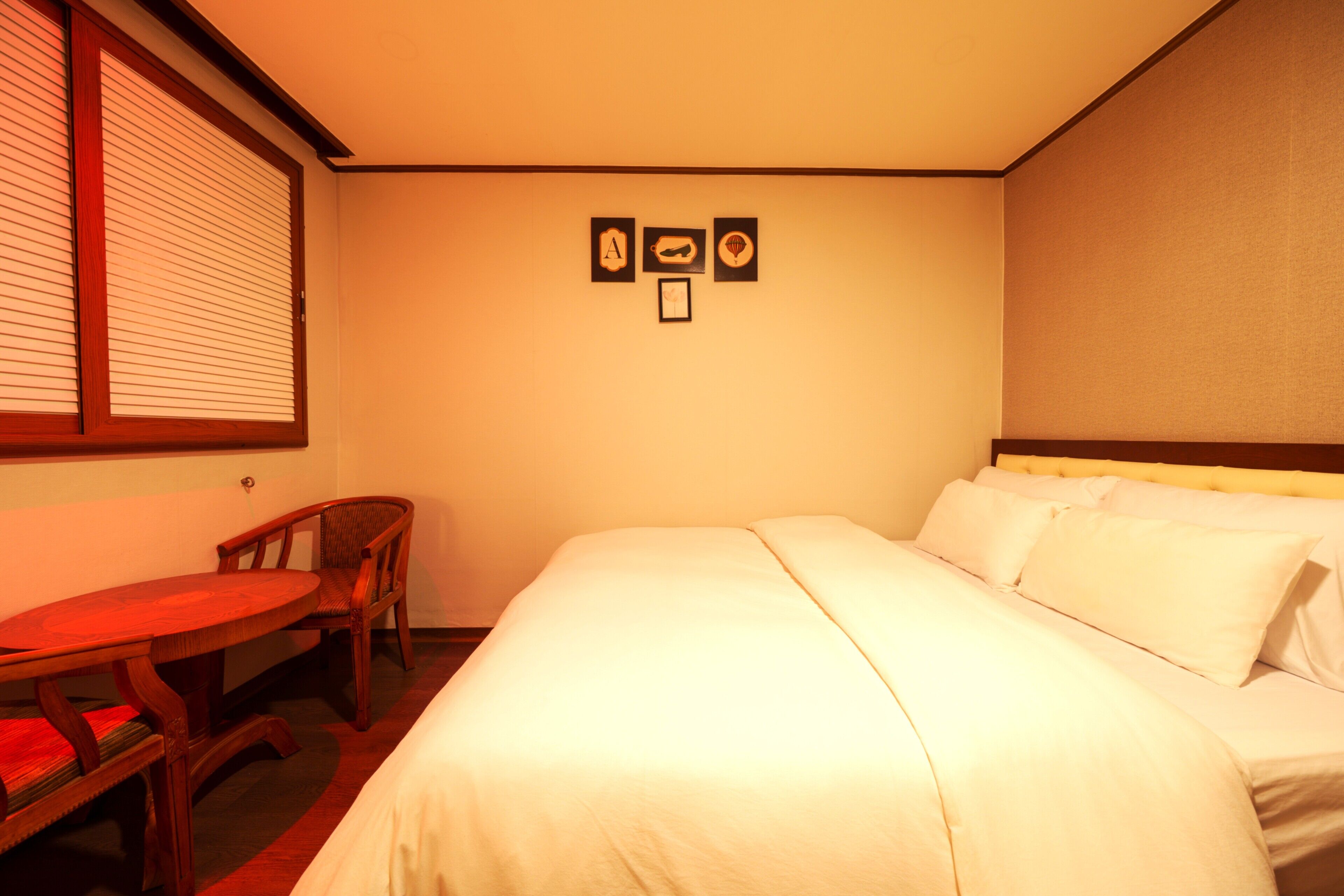 Quarto de hotel com uma cama, uma mesa pequena e duas cadeiras. Há três quadros na parede.