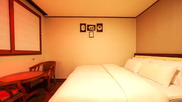 Quarto de hotel com uma cama, uma mesa pequena e duas cadeiras. Há três quadros na parede.