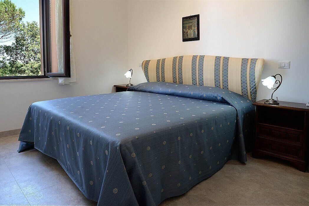 A bedroom with a bed, two bedside tables, a window, and a wall-mounted picture.