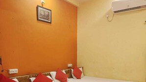 Une chambre avec un lit simple, une tête de lit en bois, un ventilateur de plafond, un appareil de climatisation et un tableau encadré au mur.