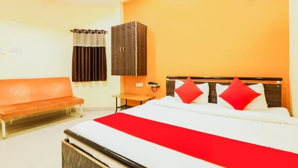 Une chambre d’hôtel avec un lit, une banquette, une armoire et une fenêtre avec des rideaux.