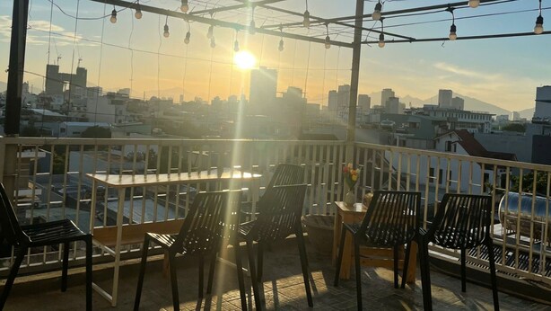 A balcony with chairs and tables, overlooking a cityscape with buildings and a body of water. - BOO BEACH Hostel, 24-Hour Reception & Free Billiards (Da Nang)