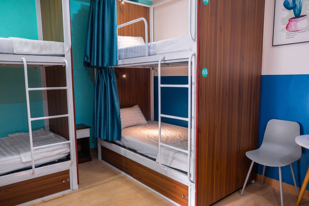 A bunk bed room with a wooden wardrobe, a small table, and a chair.