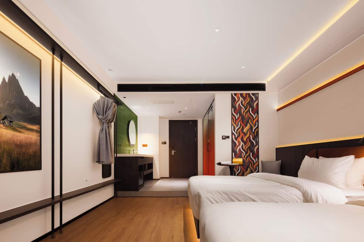 A modern hotel room with a large bed, a desk with a chair, a mirror, and a painting on the wall.