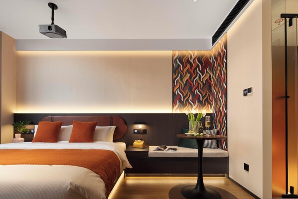 Une chambre d’hôtel moderne avec un grand lit, une table de chevet et un projecteur fixé au mur.